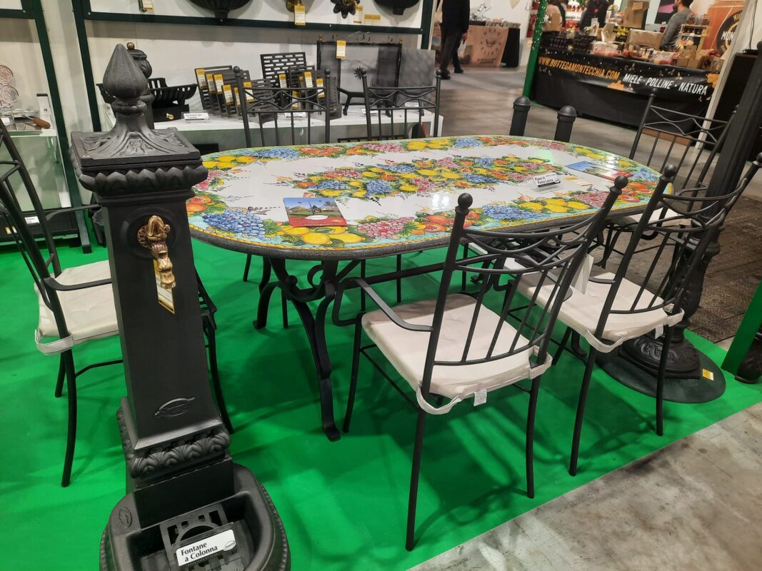 composizione di tavolo in pietra lavica dipinto a mano in mostra , sedie in ferro e fontana all'Artigiano in Fiera 2024 Milano Rho Fiera